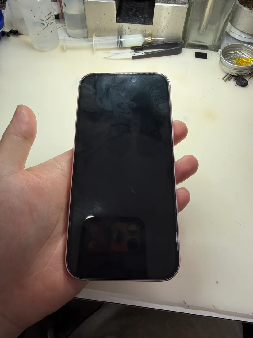 粉紅色 iPhone 15 螢幕全黑無反應，手持於維修工作檯前