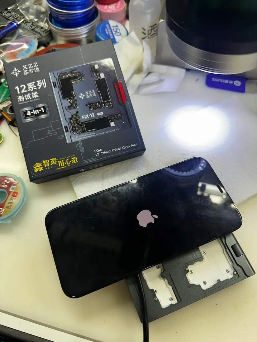一台 iPhone 卡在亮蘋果畫面,旁邊放著主機板分層治具的包裝盒