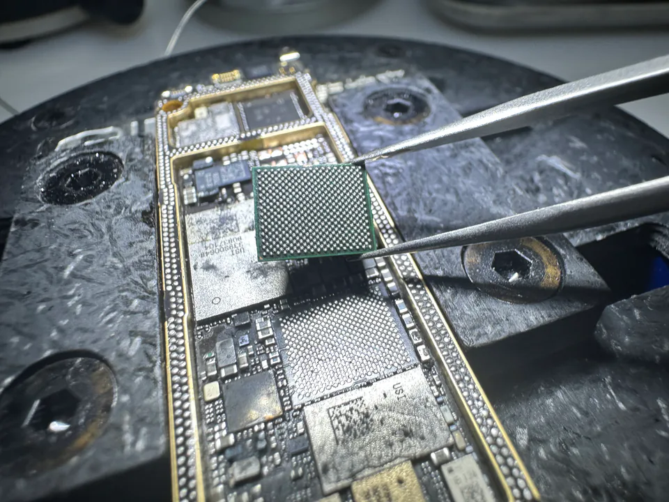 維修技師用鑷子夾取 BGA 晶片，準備對位放回 iPhone 主機板上